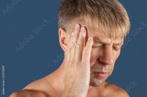 A man holds his hands on his head on blue background. Headache or migraine.