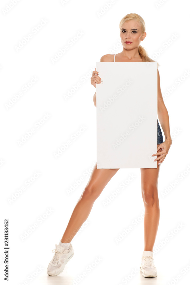 Young pretty woman posing in short jeans on white background, and holding empty board