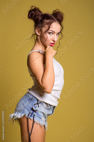 Sexy beautiful girl in denim shorts and white T-shirt on a yellow background