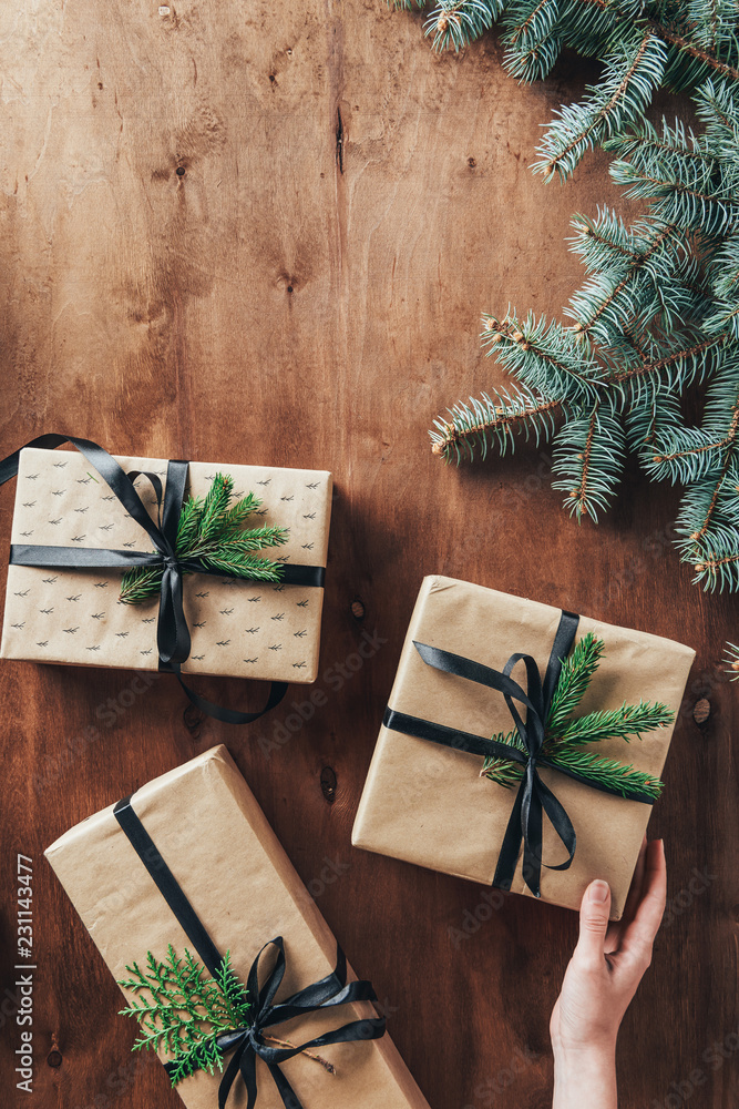 cropped view of woman touching gift boxes on wooden background with christmas tree branches cropped view of woman touching gift boxes on wooden background with christmas tree branches