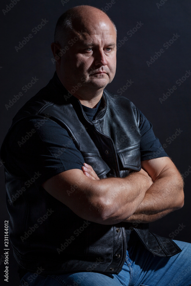 Adult brutal bald man in a leather jacket, dark background Adult brutal bald man in a leather jacket, dark background