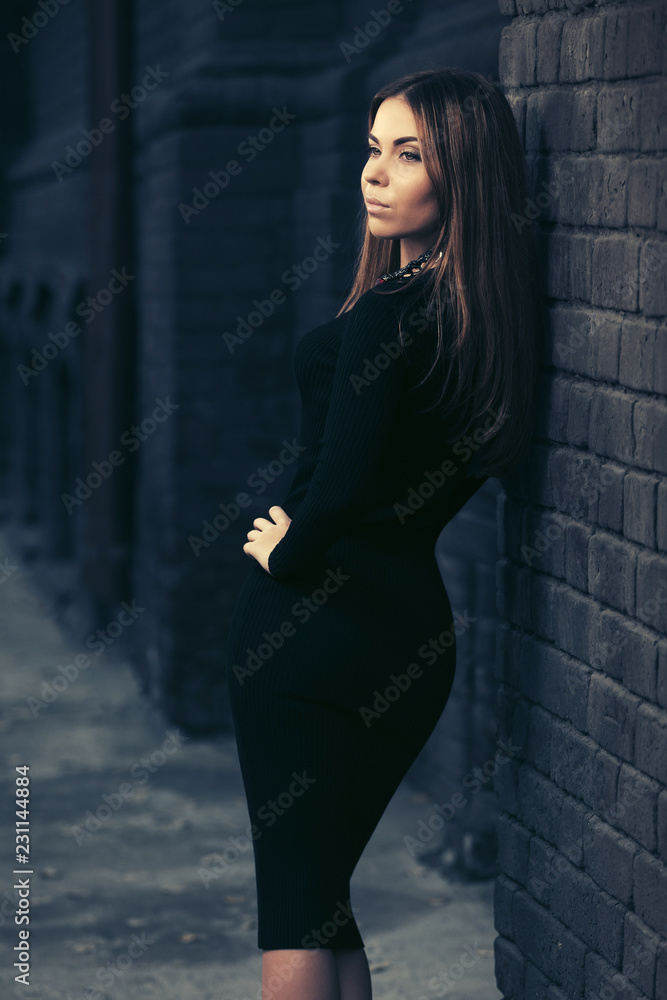 Young fashion woman in black dress leaning on brick wall