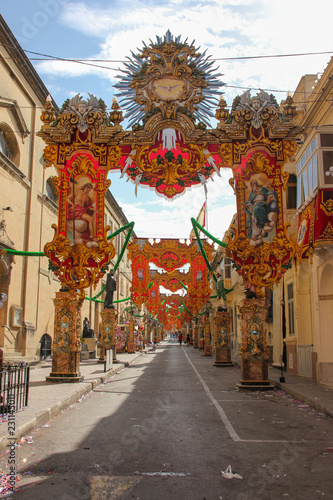 Nearly empty festively decorated street with old traditional balconies. Tunnel of banners and statues for annual festa religious holiday in Marsa, Malta