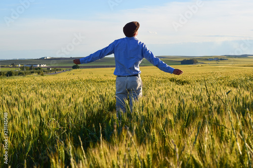 Chico joven contento de espaldas con los brazos abiertos en mitad de un campo de trigo