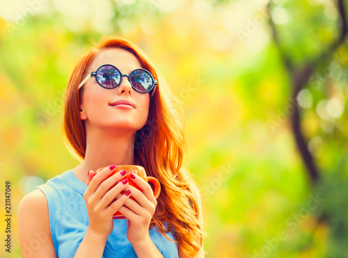 Smiling redhead girl winh cup in the autumn park. photo