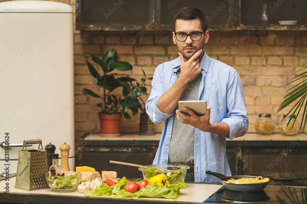 Man preparing delicious and healthy food in the home kitchen on a sunny day. Using tablet computer for searching recipes. Man preparing delicious and healthy food in the home kitchen on a sunny day. Using tablet computer for searching recipes.