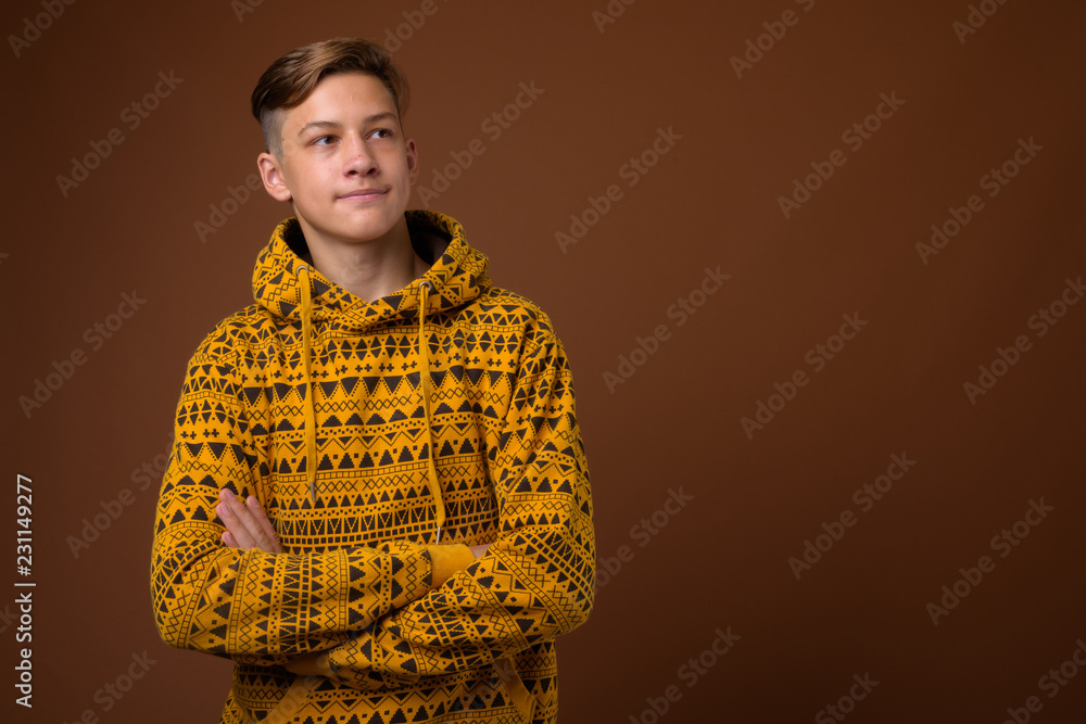 Fototapeta premium Studio shot of young handsome teenage boy against brown backgrou