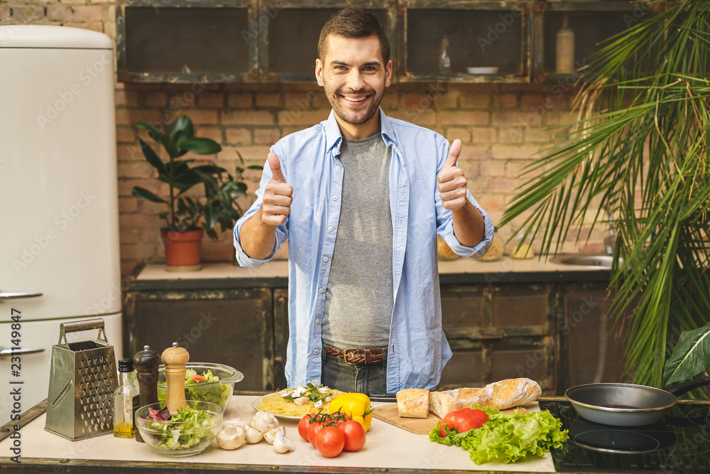 Portrait of young man preparing delicious and healthy food in the home kitchen on a sunny day. Thumbs up. Portrait of young man preparing delicious and healthy food in the home kitchen on a sunny day. Thumbs up.