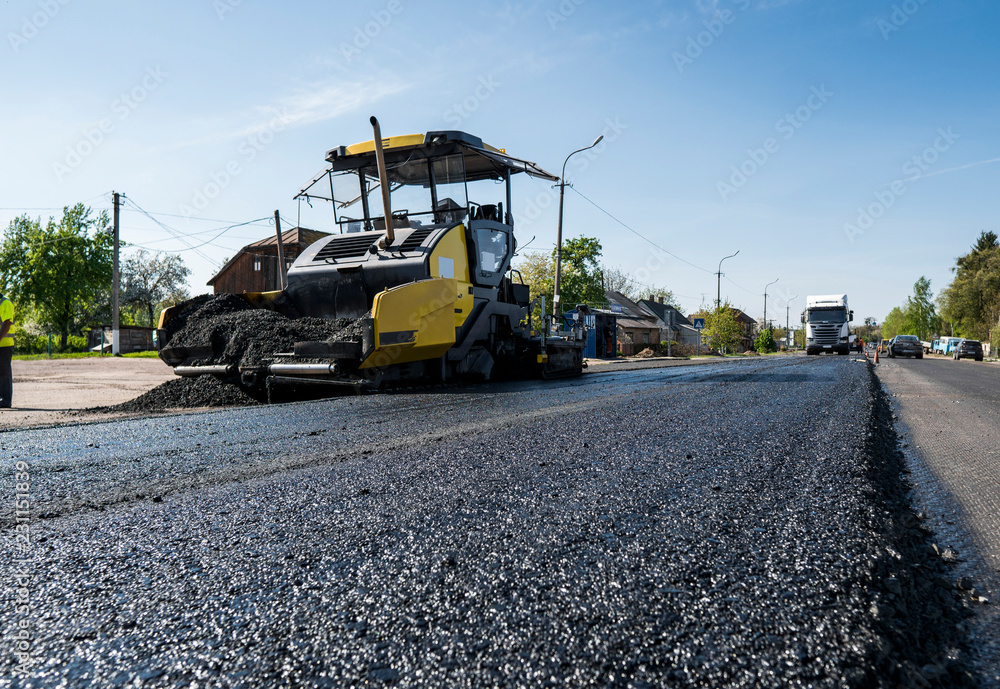 Worker operating asphalt paver machine during road construction and repairing works. A paver finisher, asphalt finisher or paving machine placing a layer of asphalt. Repaving Worker operating asphalt paver machine during road construction and repairing works. A paver finisher, asphalt finisher or paving machine placing a layer of asphalt. Repaving