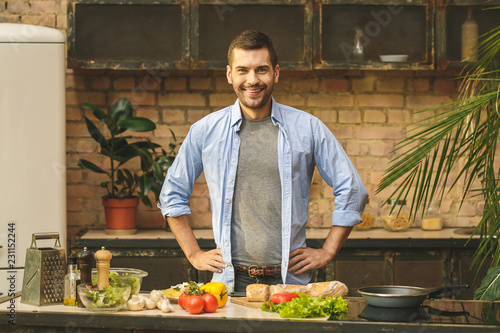 Portrait of young man preparing delicious and healthy food in the home kitchen on a sunny day. Smiling and looking at camera.