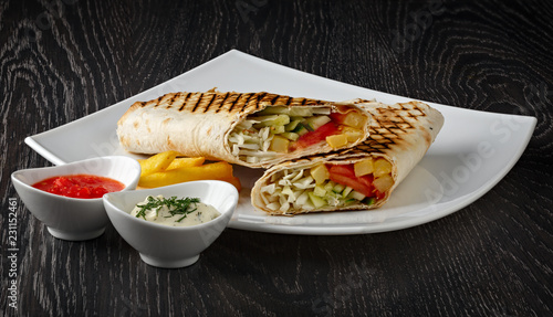 Shawarma in pita bread is cut and lies on a white plate. The Middle Eastern dish is prepared on the grill and served with sauce.