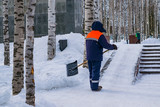 A man in work clothes with a shovel removes snow from the track in the Park in the winter landscape
