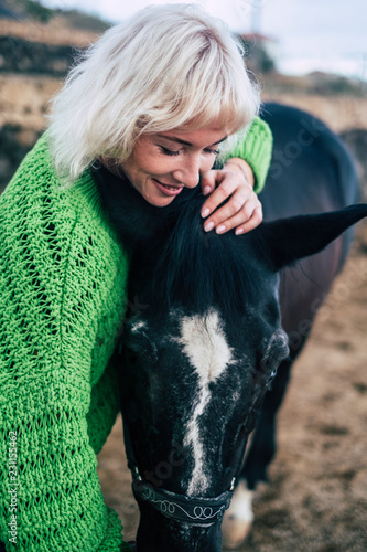 Love concept for people and animlas together in happiness and friendship. beaitufl blonde woman and dark horse in outdoor scenic place hugging and loving photo