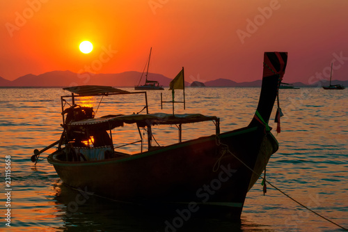 Silhouette of a longtail fisherman boat on the seafront in bright colorful orange sun color at sunset. Tropical horizon with islands and catamarans. Sunset at the Railay Beach. Krabi, Thailand. photo