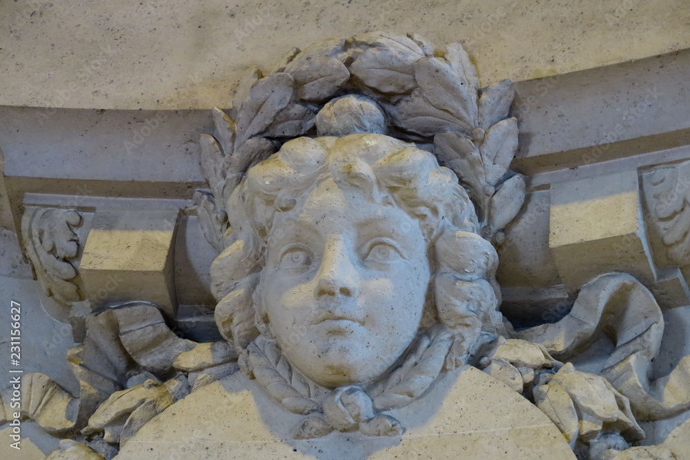 Visage de femme sculpté en pierre blanche sur façade