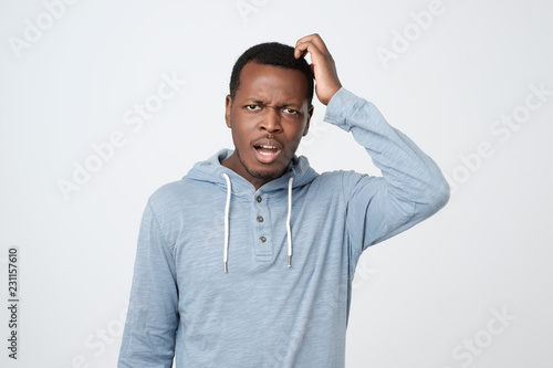 Young african man in blue shirt thinking scratching head on white background