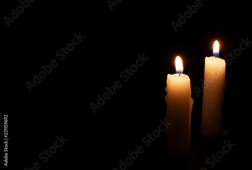 Two candles on black background. Lighting candles in darkness. Yellow wax candle with warm flame. In memoriam banner photo