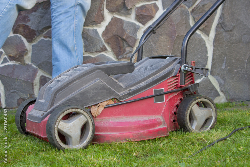 Fototapeta premium old lawn mower,The red mower is old on the green grass in the fall