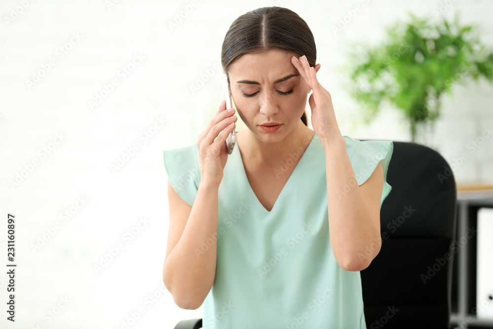 Woman suffering from headache while talking by mobile phone in office Woman suffering from headache while talking by mobile phone in office