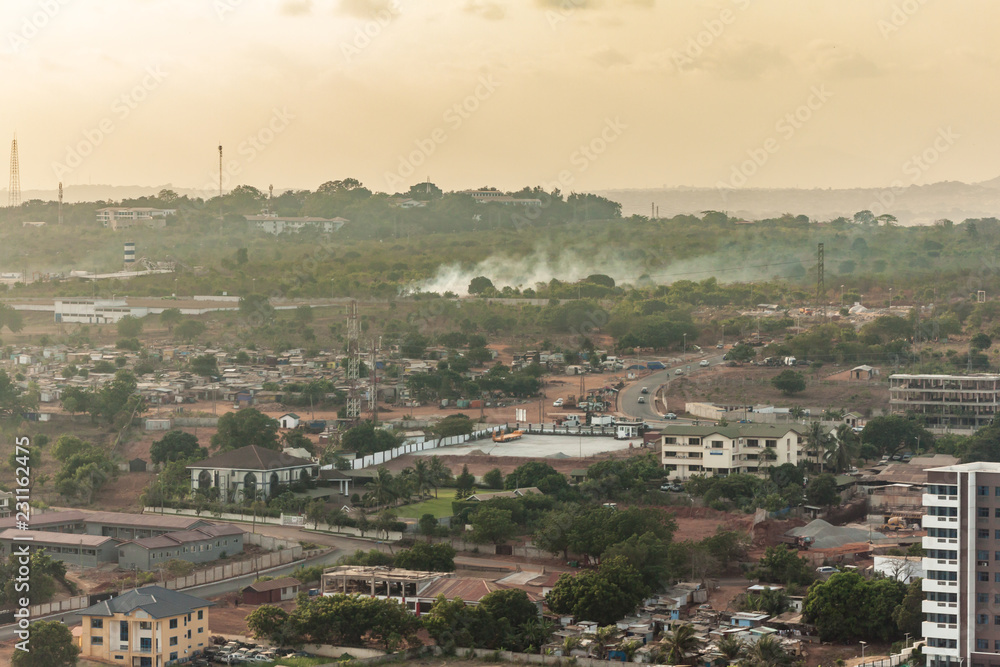 High view point cityscape of a neighborhood  in de hills of Accra, Ghana. Apartment buildings, slums, construction sites, wastelands and streets . Smoke from burning waste with a green and hazy horizo