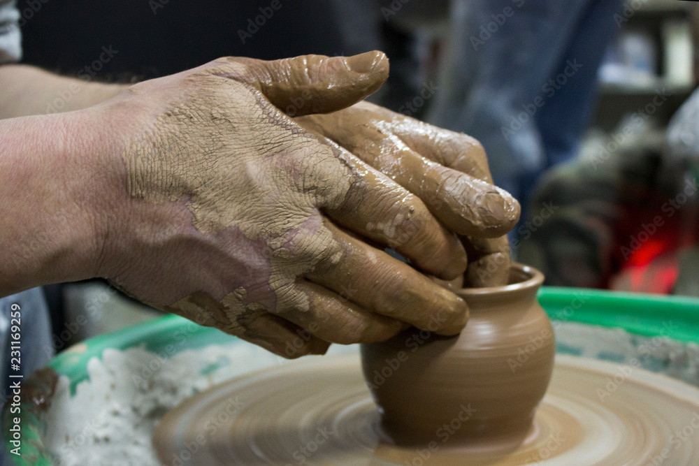 male hands of a student in pottery training courses, reportage photography. making a pot of red clay on a potter's wheel.