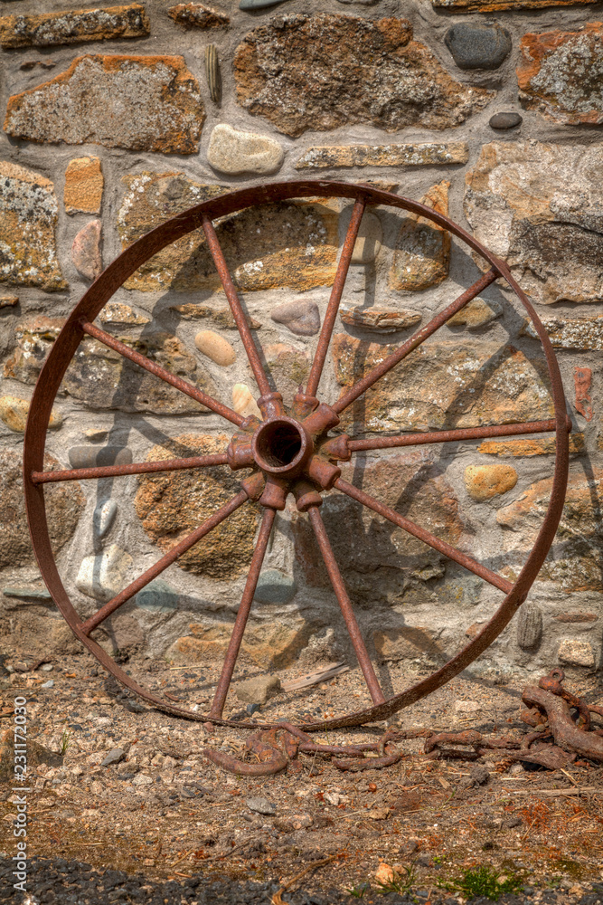Rusty cart wheel resting against a stone wall no. 2