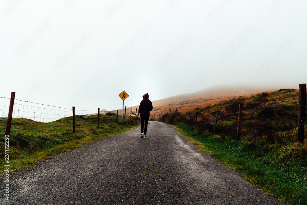 Young woman on hoodie walks on misty road