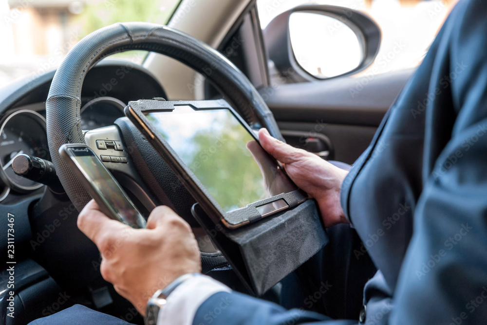 Businessman working on tablet and smartphone inside car on bright day