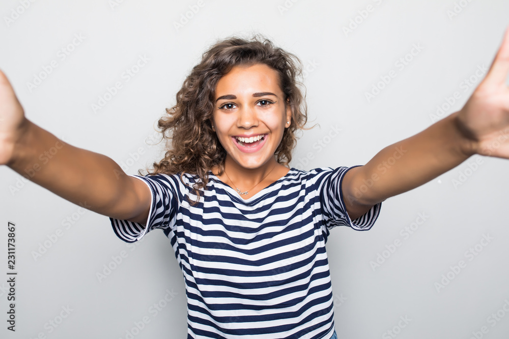 Portrait of a smiling young mixed race woman taking selfie with mobile phone over gray background Portrait of a smiling young mixed race woman taking selfie with mobile phone over gray background