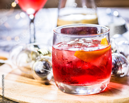 A red coloured cocktail with ice cubes and a twist of lemon 