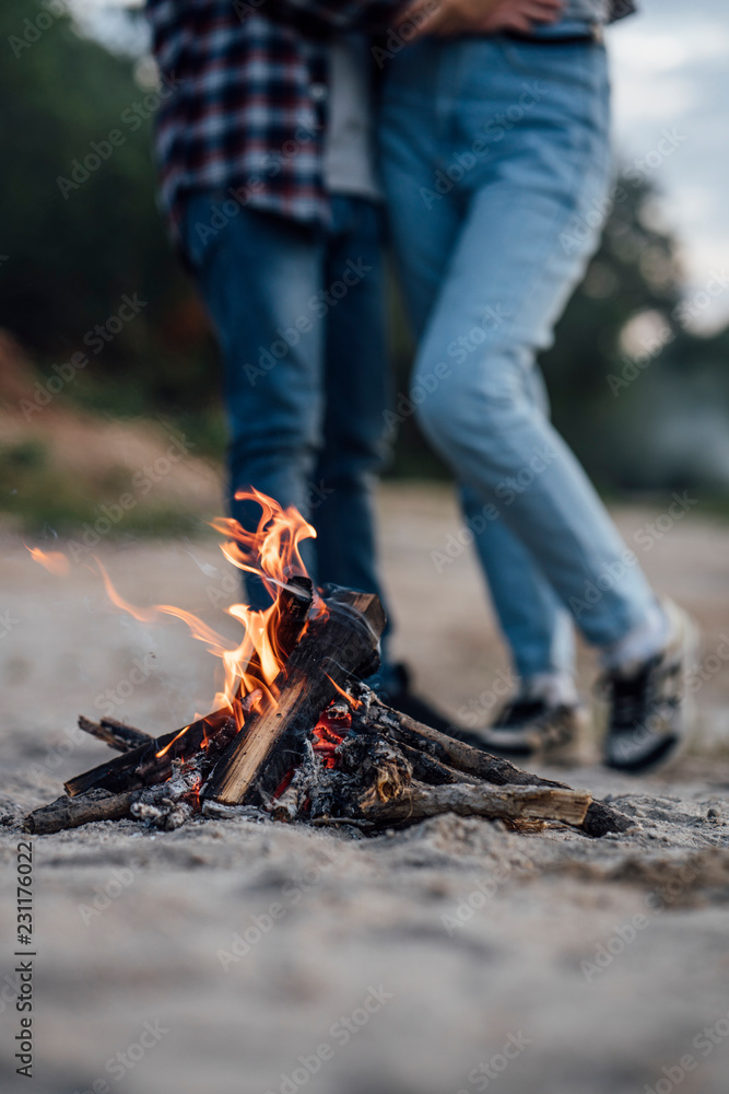 Burning campfire at the riverside, couple in background Burning campfire at the riverside, couple in background