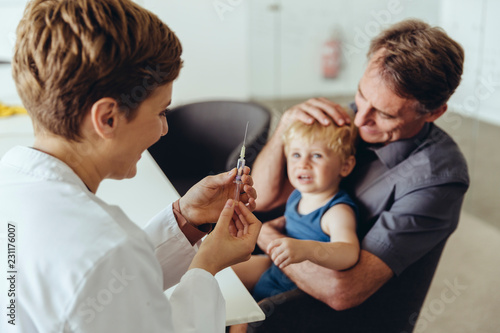 Father holding son while being vaccinated by pediatrician
