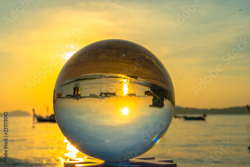 crystal glass ball sphere reveals sunrise seascape with spherical perspective on the beach in Phuket island.