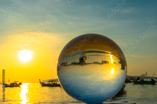 crystal glass ball sphere reveals sunrise seascape with spherical perspective on the beach in Phuket island. © Narong Niemhom