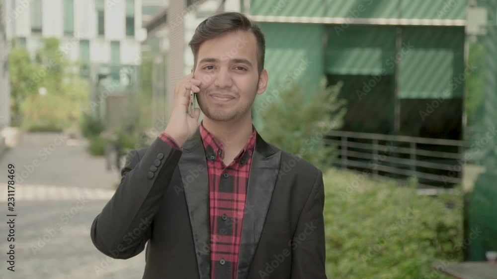 Happy Indian young man talking on phone with smile. Interested South Asian guy sharing good news. Pleasant communication concept Happy Indian young man talking on phone with smile. Interested South Asian guy sharing good news. Pleasant communication concept