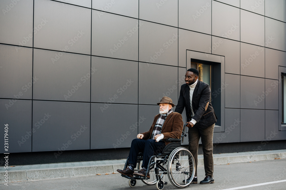 senior disabled man in wheelchair and young african american cuidador riding by street senior disabled man in wheelchair and young african american cuidador riding by street
