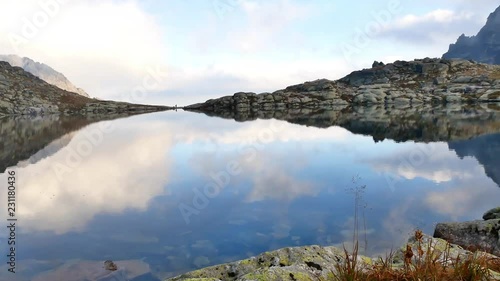 Pan over the mountain lake Spisske pleso, reflecting the blue sky and a perosn walking in the distance. (high tatras, slovakia)  photo