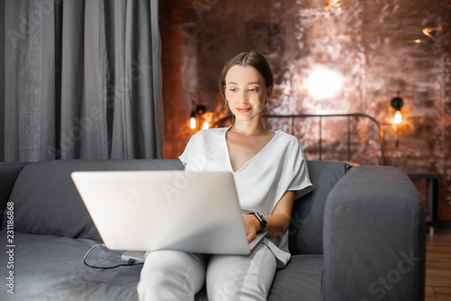 Young woman in white clothes sitting on the couch with laptop at the living room of the modern loft apatment photo