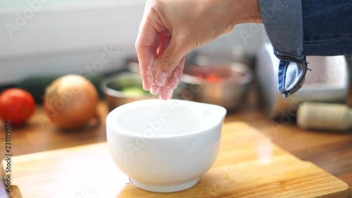 Woman adding salt or spices into bowl in kitchen