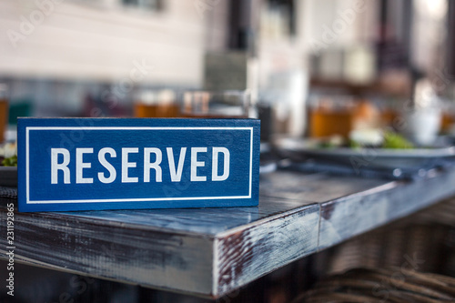 A wooden blue and white rectangular plate with the inscription Reserved stands on the corner of a gray aged vintage table. Concept of lunch in a restaurant, holiday, banquet