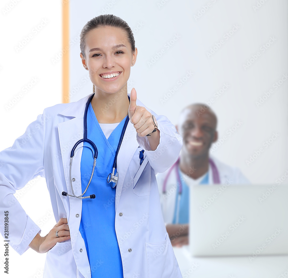 Beautiful young smiling female doctor sitting at the desk and writing.