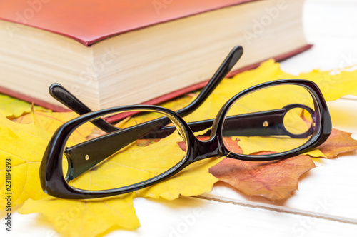 Eyeglasses with book and autumn leaves on the table. Close up.