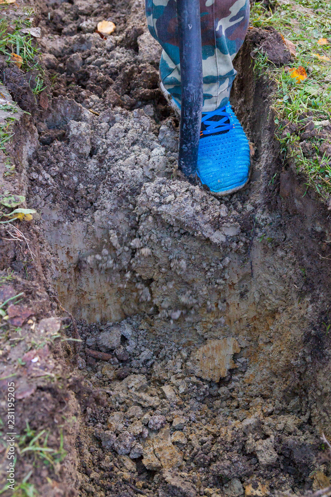 Fototapeta premium Man digging a ditch with a shovel in autumn
