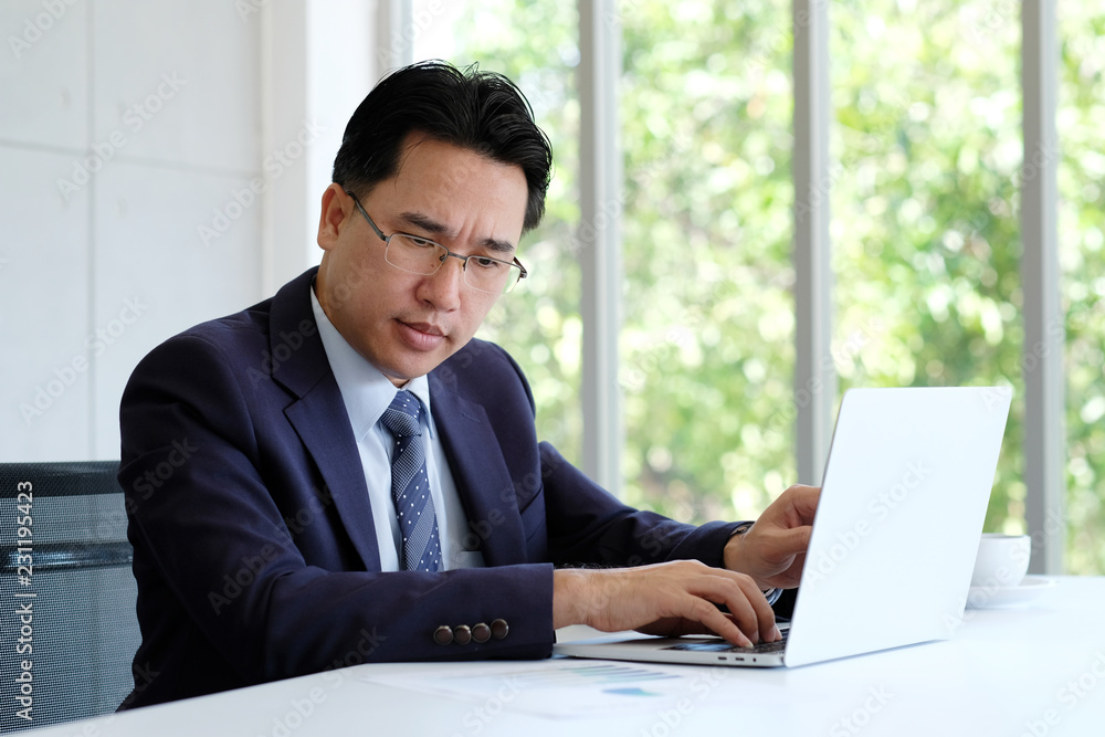 Asian businessman reading papers and working with laptop computer at office, business concept Asian businessman reading papers and working with laptop computer at office, business concept