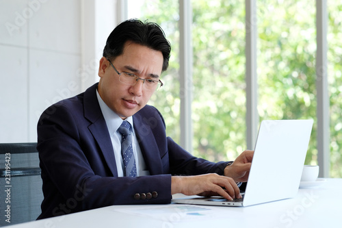 Asian businessman reading papers and working with laptop computer at office, business concept