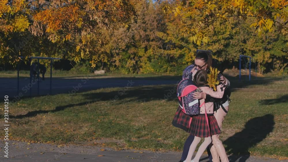 A happy mother meets her two daughters from school. Mom hugs and kisses her children in school uniform. Slow Motion in the Rays of the Sunset A happy mother meets her two daughters from school. Mom hugs and kisses her children in school uniform. Slow Motion in the Rays of the Sunset
