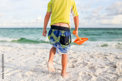 Young boy walking on the beach towards the ocean holding a shovel