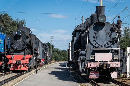 Old steam locomotive beside a railway station platform. Retro train.