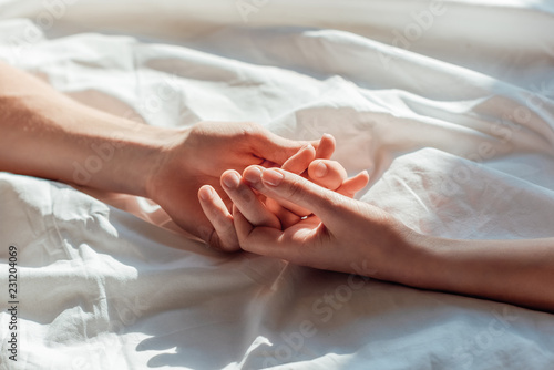 partial view of couple in live holding hads while lying in bed together photo