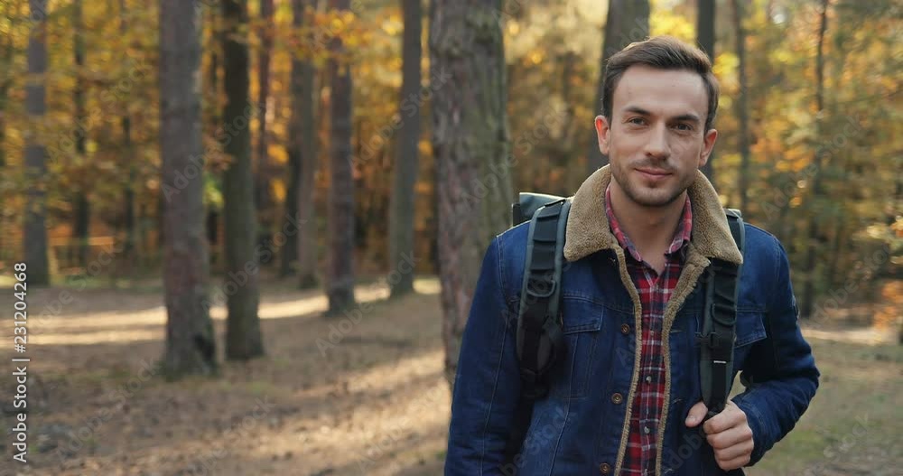 Portrait of the Caucasian attractive man tourist with a backpack looking to the camera in the middle of the autumn wood. Outdoor. Portrait of the Caucasian attractive man tourist with a backpack looking to the camera in the middle of the autumn wood. Outdoor.